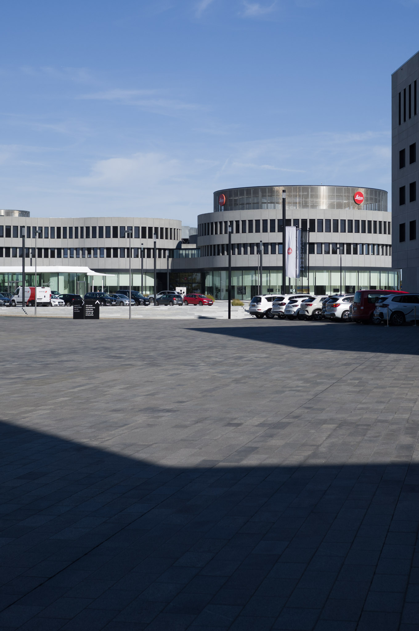 Wide view of the Leica headquarters complex with parked cars and blue sky.