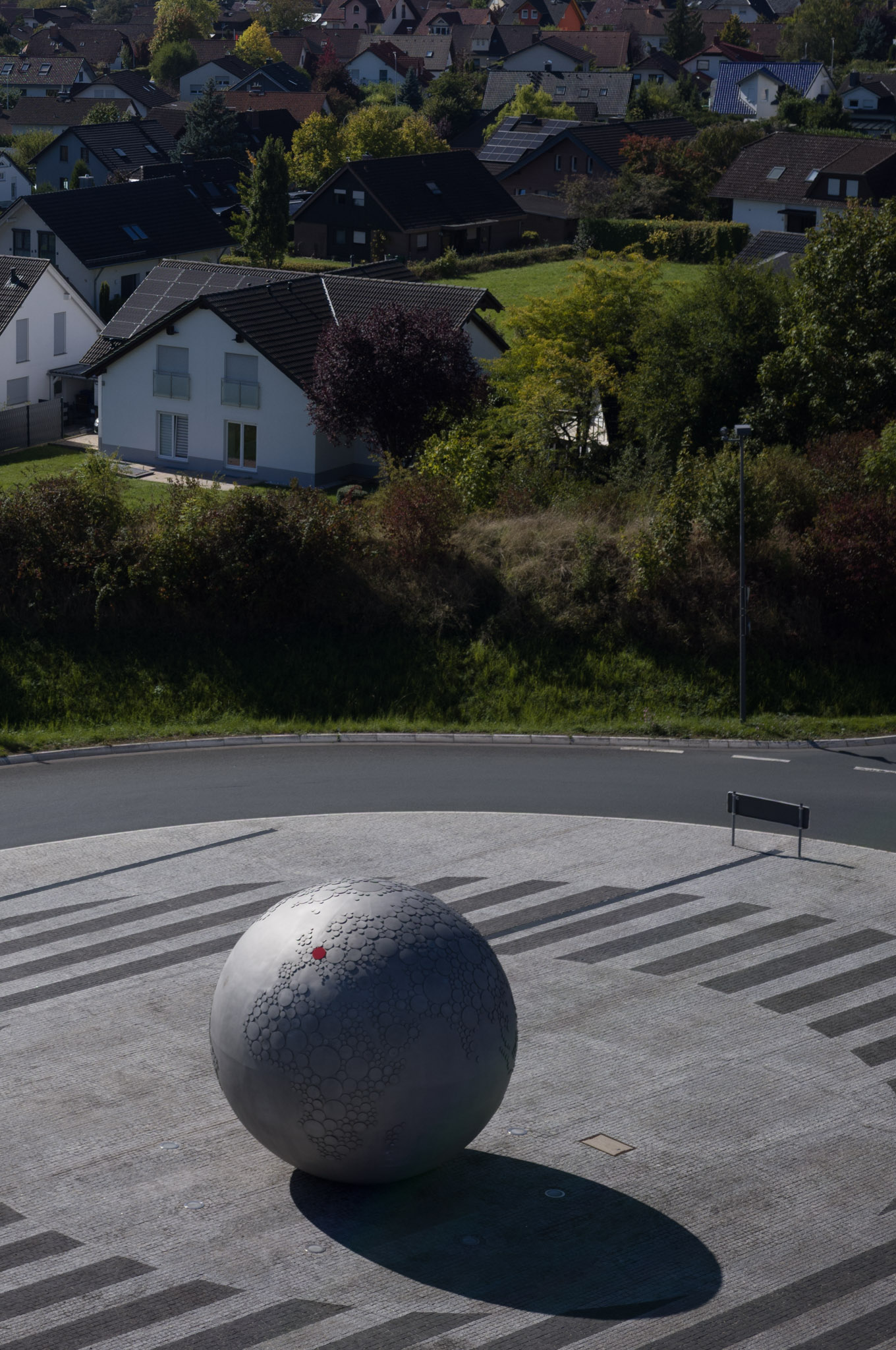 Sculptural globe centerpiece at a roundabout near residential houses.